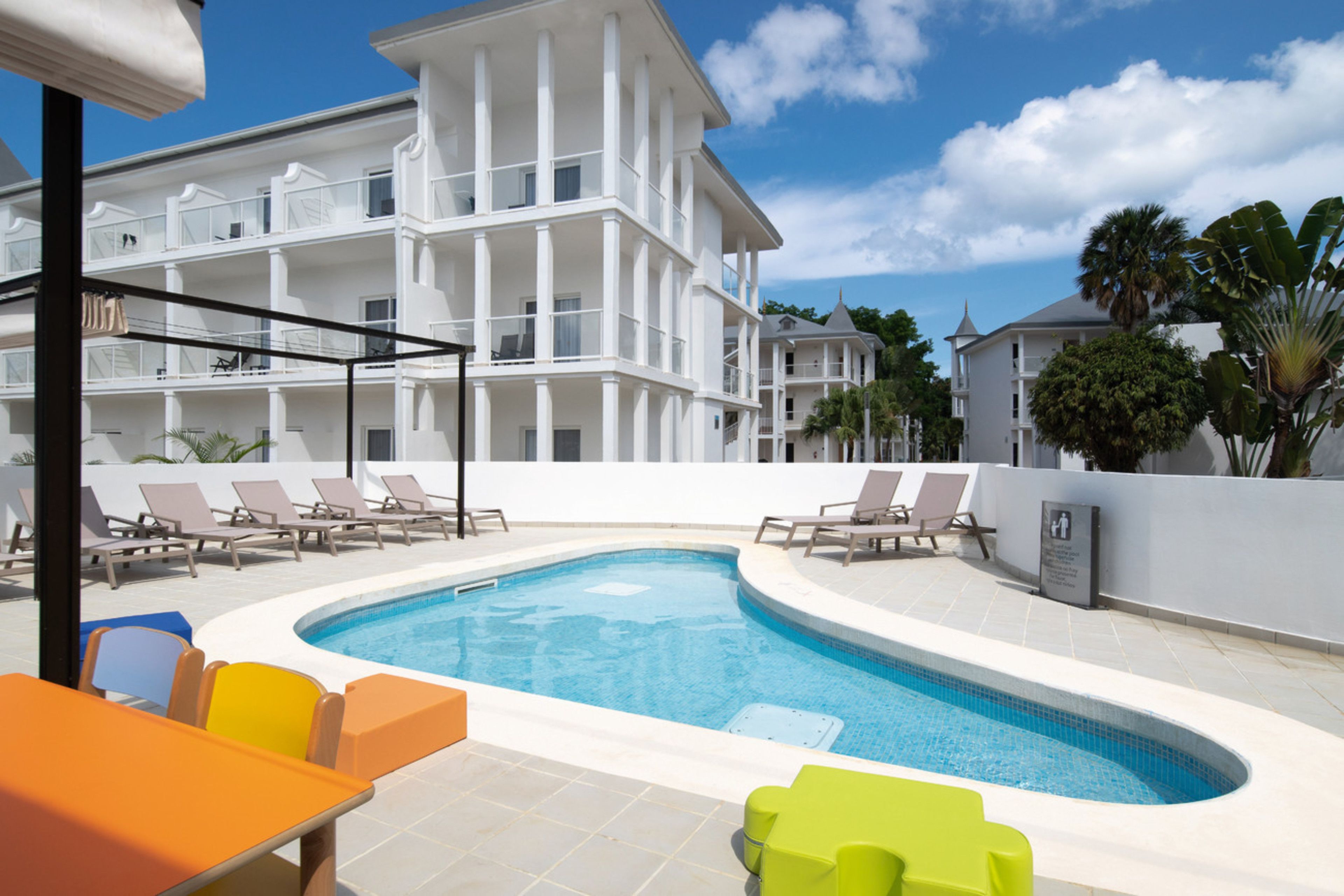 A swimming pool with lounge chairs and a multi-story building in the background.