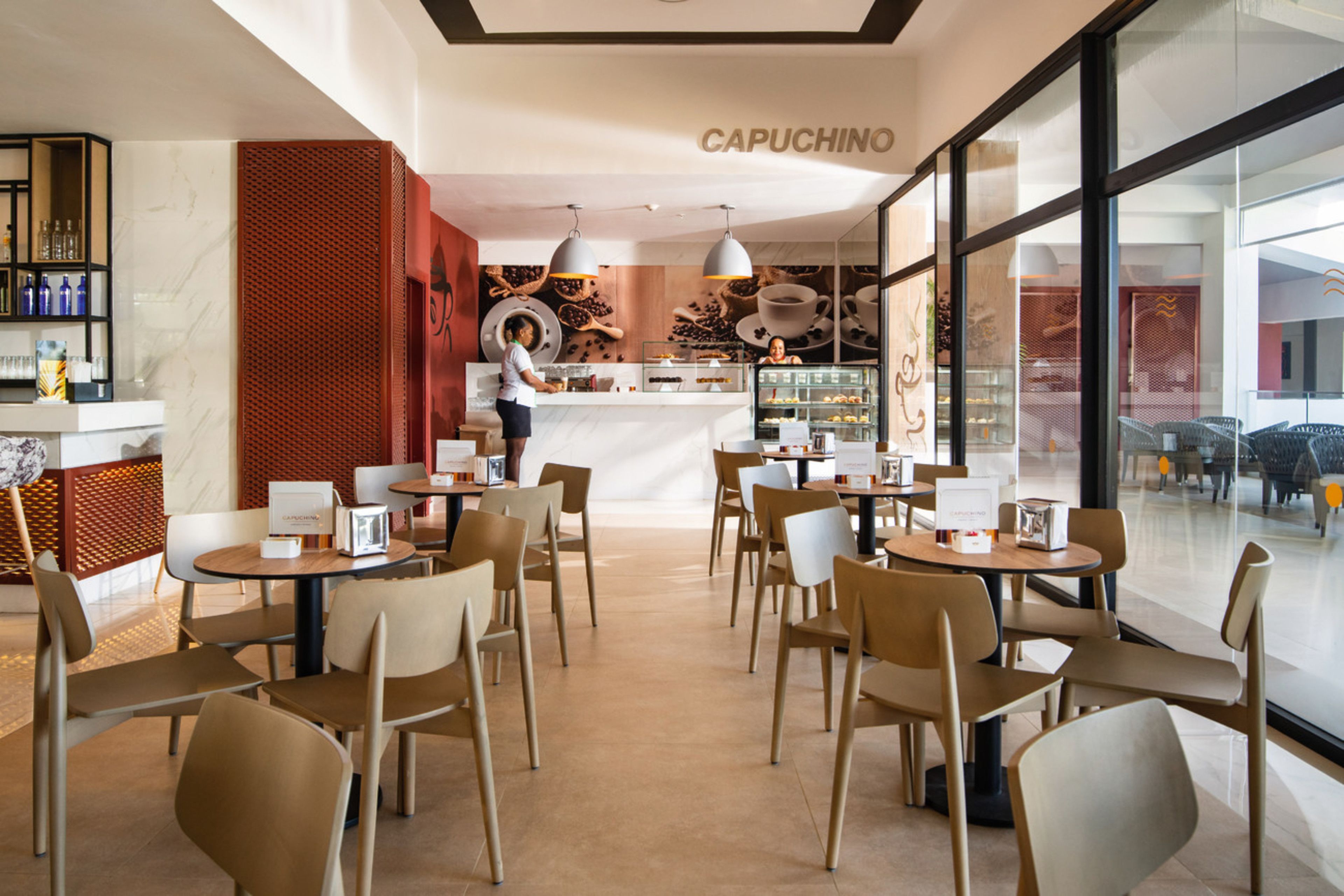 Een modern café interieur met ronde tafels en stoelen, een toonbank met een barista en een groot raam met uitzicht op de straat.