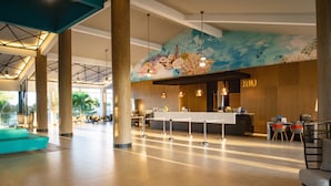 A spacious lobby with a reception desk, seating areas, and a large mural on the wall. - Hotel Riu Palace Tropical Bay - All Inclusive (Negril)