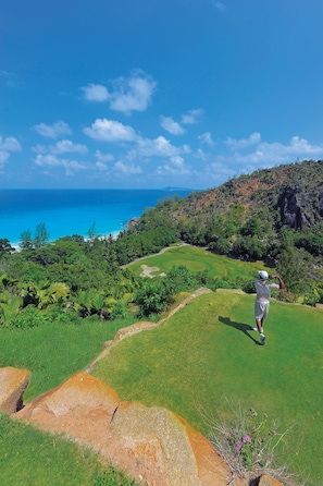 A golf course with a view of the ocean and a hilly landscape.