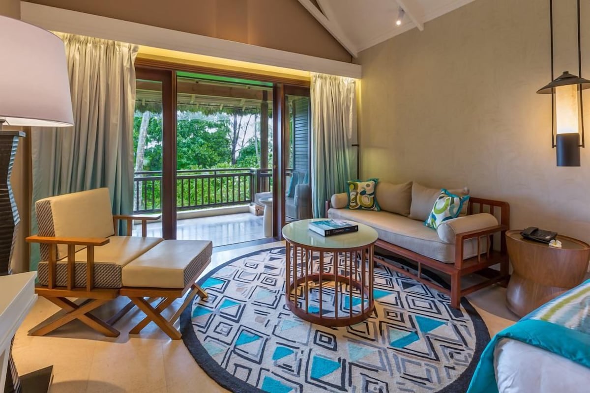 A hotel room with a balcony, a sofa, a chair, a coffee table, and a lamp.