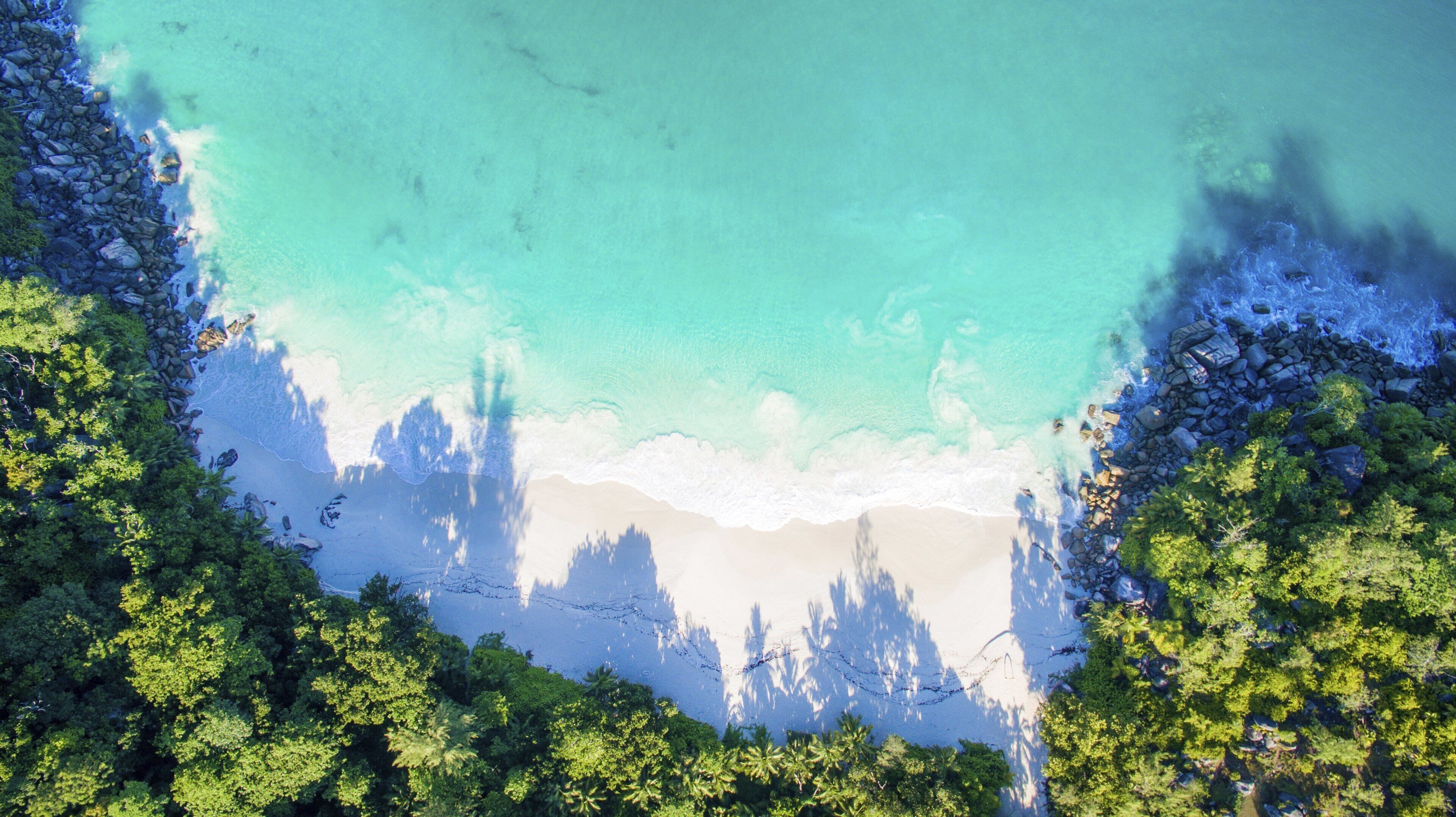 A beach with clear turquoise water, surrounded by dense green forest and rocky outcrops.