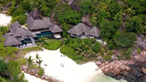 Vista aérea de um resort com villas de telhado de palha, uma piscina e uma praia.