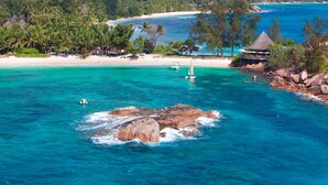 Uma praia tropical com águas turquesa cristalinas, um afloramento rochoso e uma pequena cabana na costa.