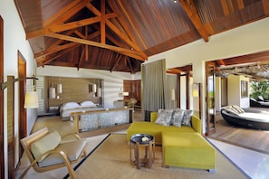 A spacious room with a large bed, a yellow sofa, and a dining area.