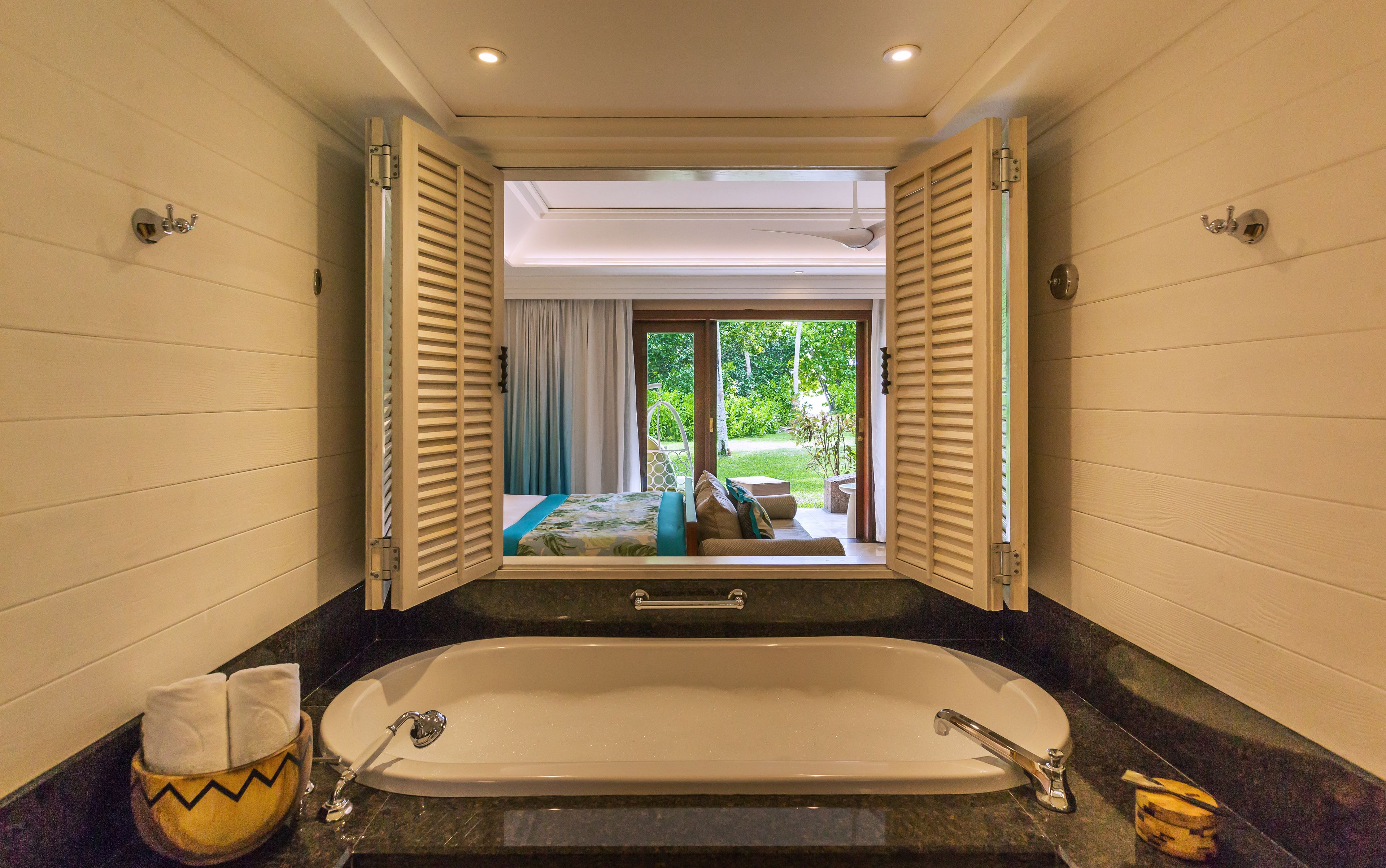 Une salle de bain avec une baignoire, une serviette et une vue sur un jardin extérieur, accessible par une porte coulissante.
