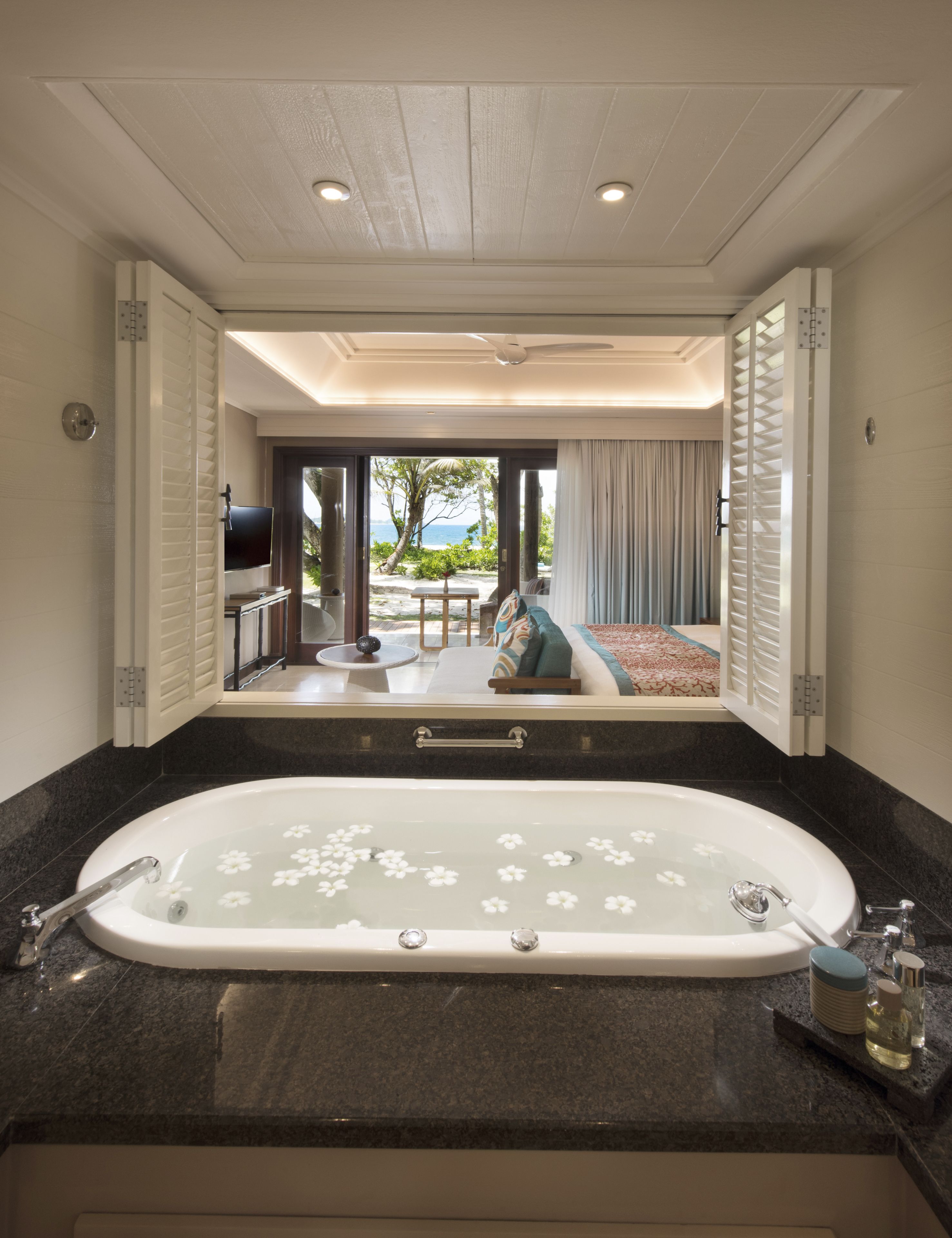 A bathroom with a large bathtub, a mirror, and a view of an outdoor seating area.
