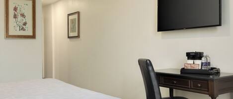 Habitación de hotel con cama, escritorio con silla, televisor de pantalla plana y cuadros en la pared.