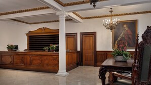 A formal reception area with a wooden reception desk, a chandelier, and a large portrait on the wall.