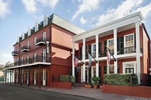 Un hotel de dos pisos con fachada roja, columnas blancas y balcones.