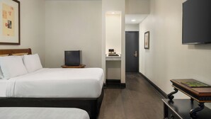 A hotel room with a bed, a television, a desk with a computer, and a door leading to a bathroom.