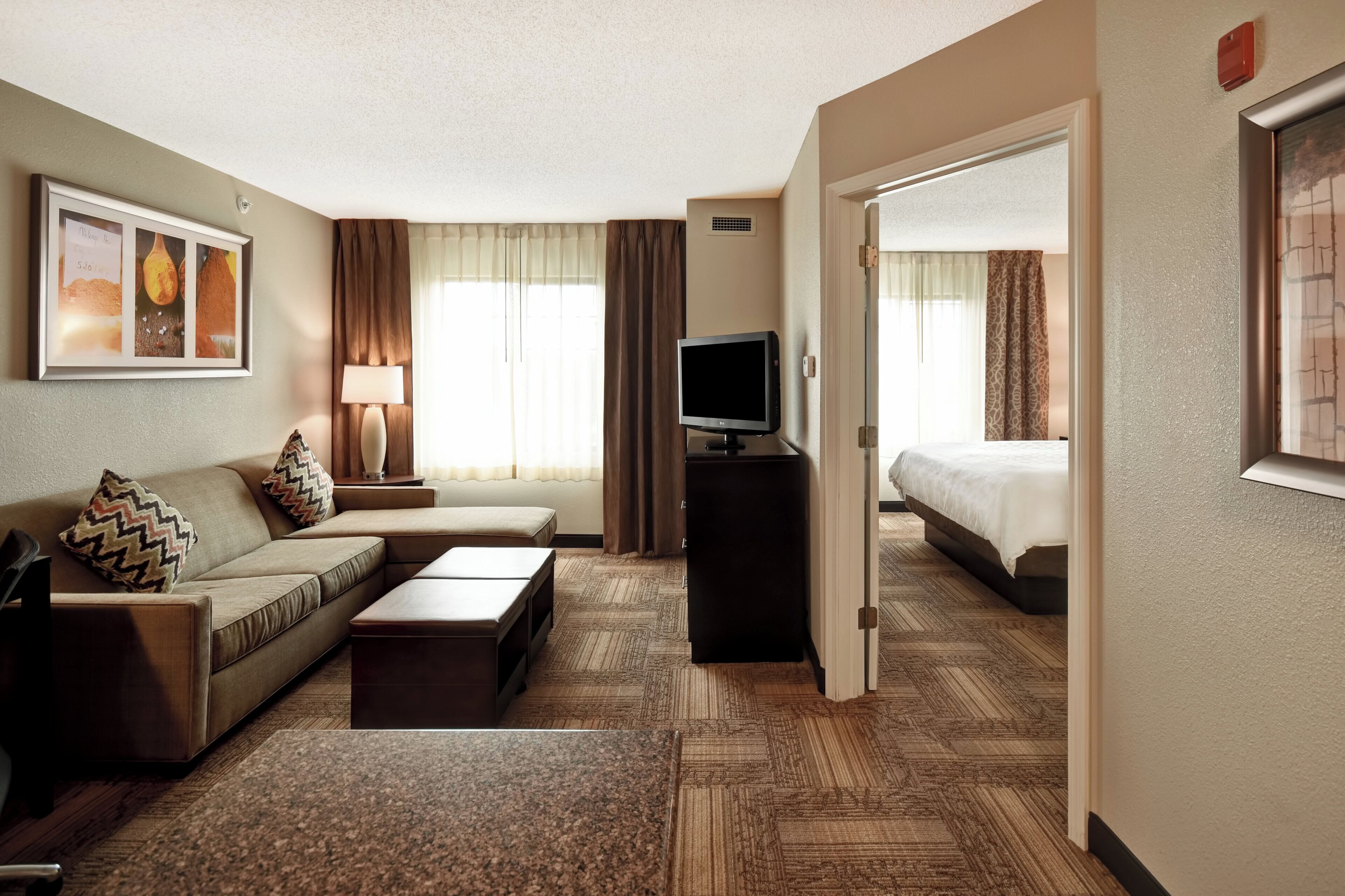 Quarto de hotel com sofá, televisão, cama e piso coberto por carpete.