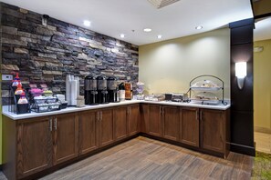 Habitación de hotel con pared de piedra, muebles de madera, estación de café y refrigerador.