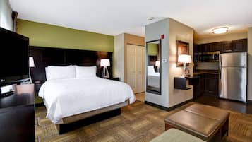 A hotel room with a bed, bedside table, lamp, TV, and a kitchenette with a refrigerator and microwave.