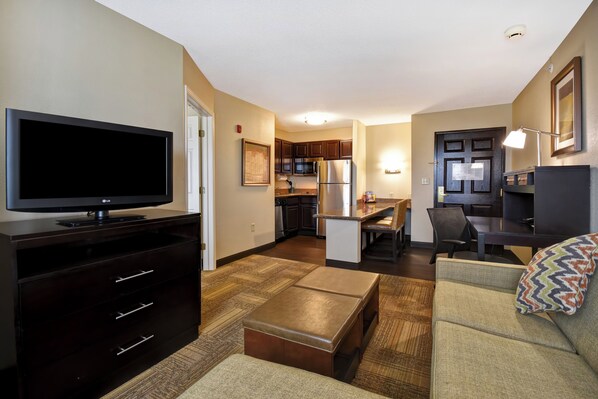 A modern apartment with a flat-screen TV, a dining area, kitchen, and a living room with a sofa and ottoman.