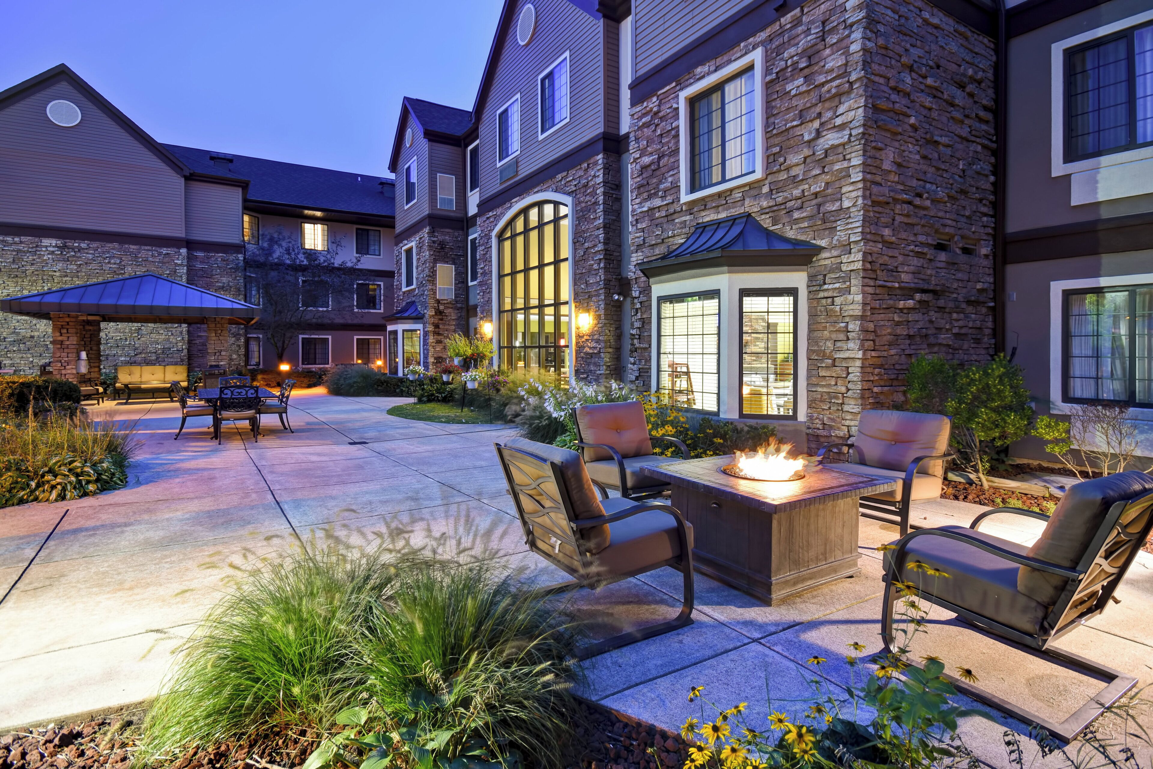 Une maison à étages avec une façade en pierre, un patio doté de mobilier d’extérieur et un foyer.