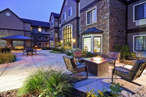 Una casa de varios pisos con fachada de piedra, un patio con mobiliario exterior y una chimenea.