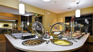 Mostrador de buffet con diferentes alimentos y una mampara de vidrio.