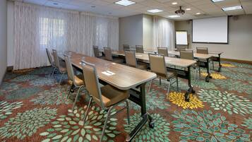 A conference room with a long table, chairs, a projector screen, and a carpet with a floral pattern.