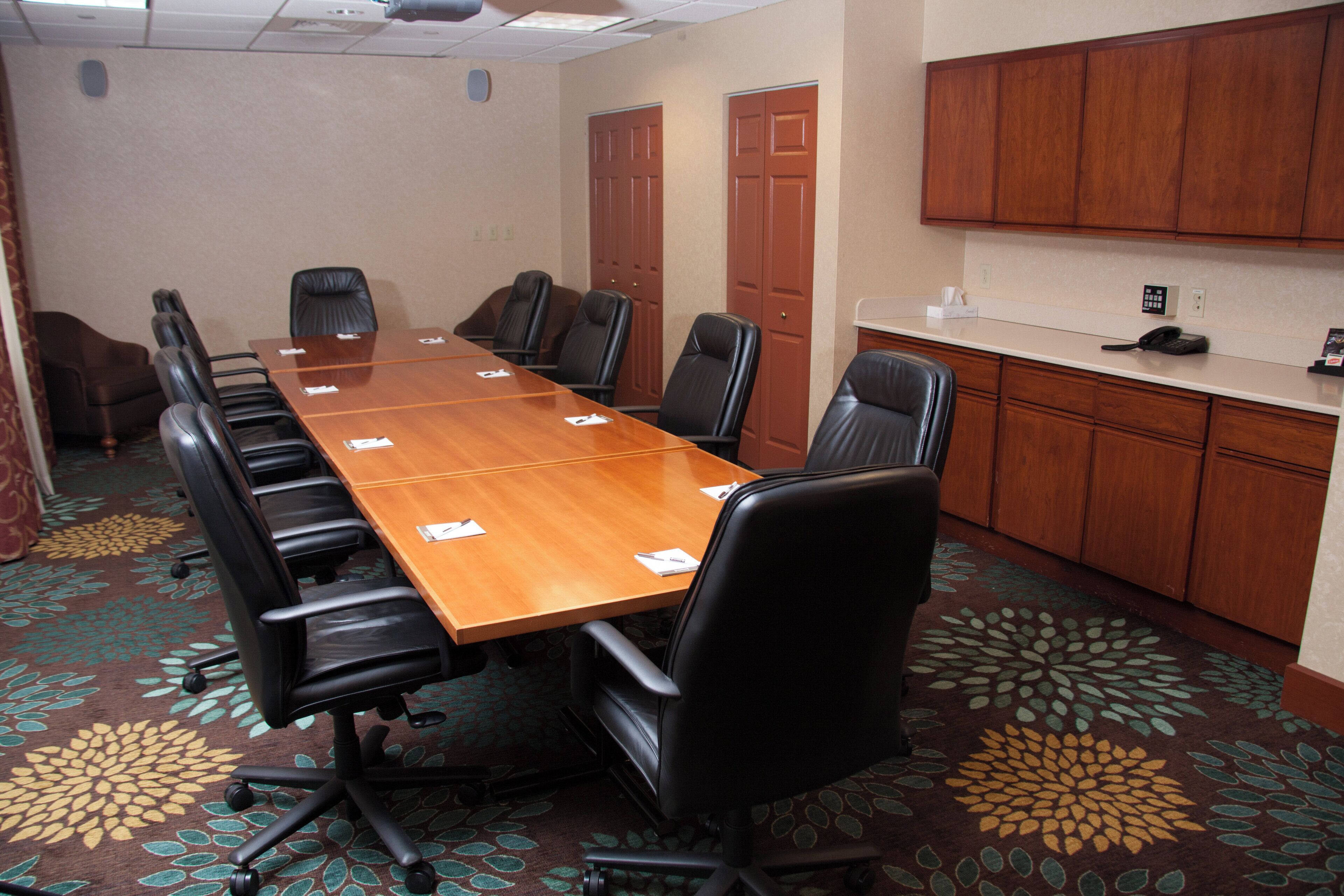 A conference room with a long table, black chairs, and a carpeted floor.