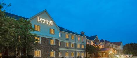 Een Staybridge Suites hotel met een gevel van natuursteen, meerdere ramen en een parkeerplaats.