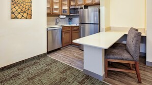 A modern kitchen with wooden cabinets, stainless steel appliances, and a dining area with a chair. - Staybridge Suites Corning by IHG (Corning)