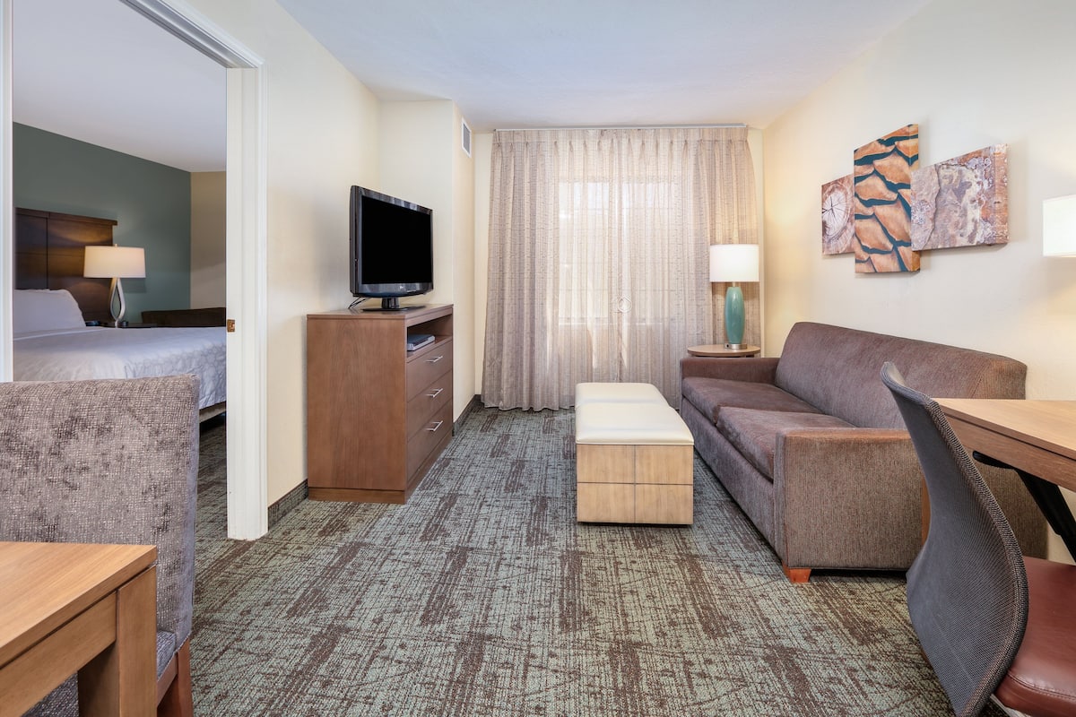 Ein Hotelzimmer mit Bett, Fernseher, Sofa, Schreibtisch und Sessel.