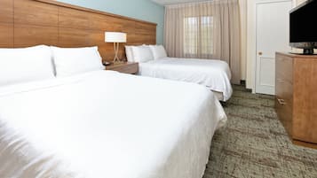 A hotel room with two beds, a nightstand, a lamp, a television, and a wooden headboard.