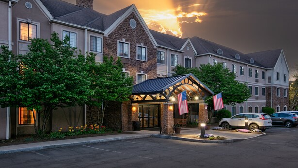 A hotel with a stone facade, multiple windows, and an American flag. - Staybridge Suites Corning by IHG (Corning)