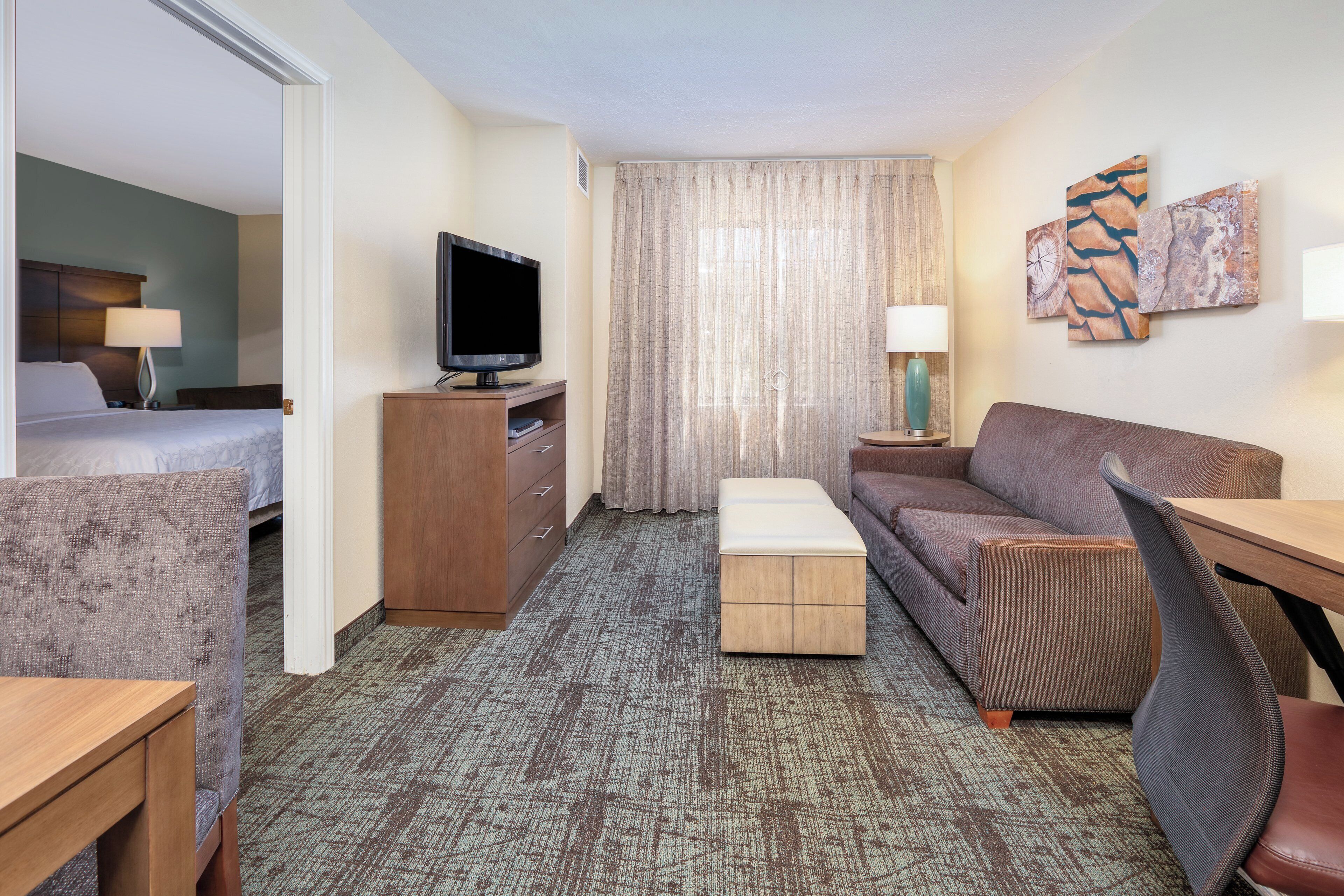 Una habitación de hotel con una cama, televisor, escritorio, sofá y una mesita.