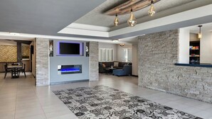 A spacious living area with a stone wall, a fireplace, a modern sofa, and a dining area with a table and chairs. - City Express By Marriott Manhattan Beach (Manhattan Beach)
