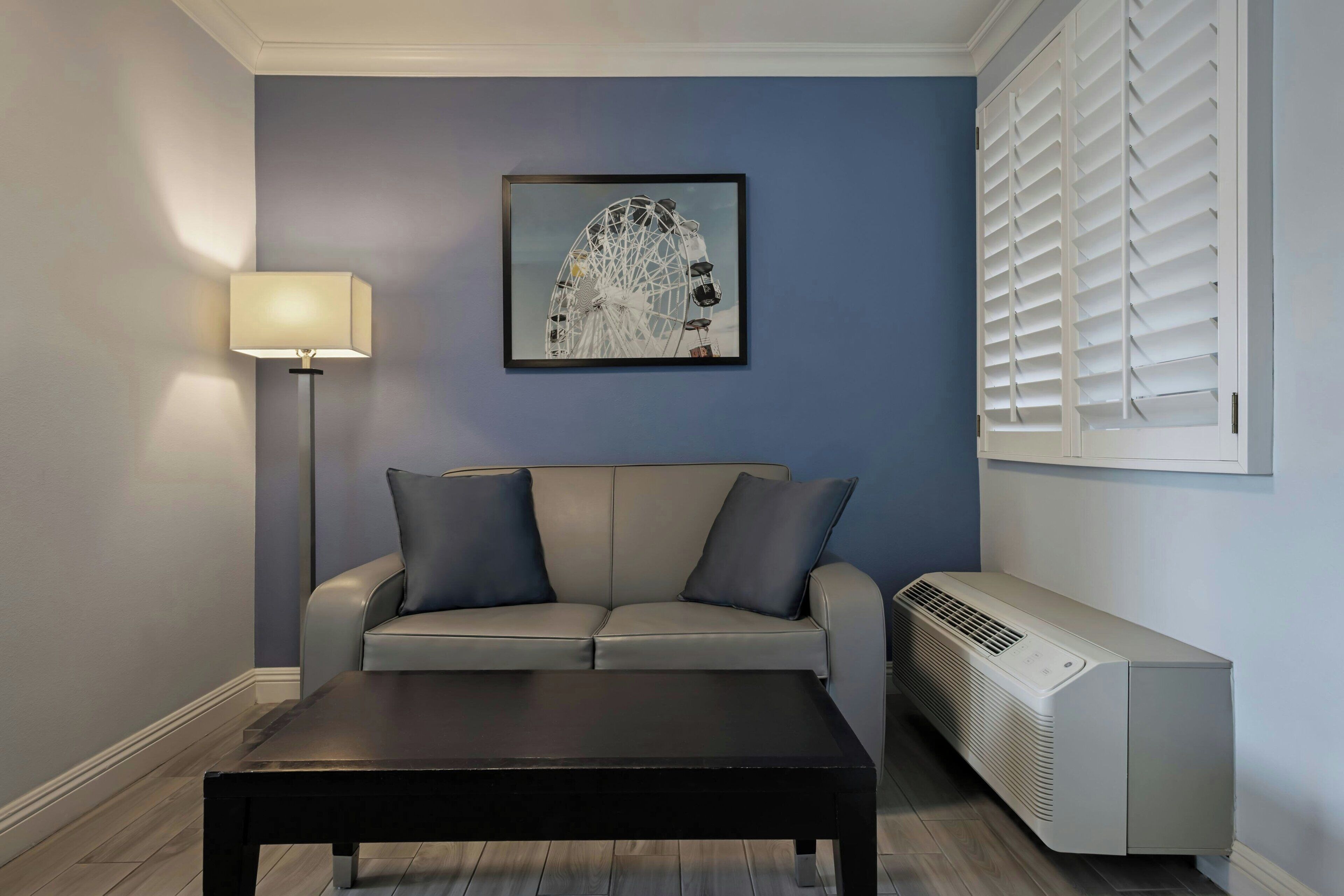 Uma sala de estar com sofá, mesa de centro, luminária, quadro na parede e ar condicionado.