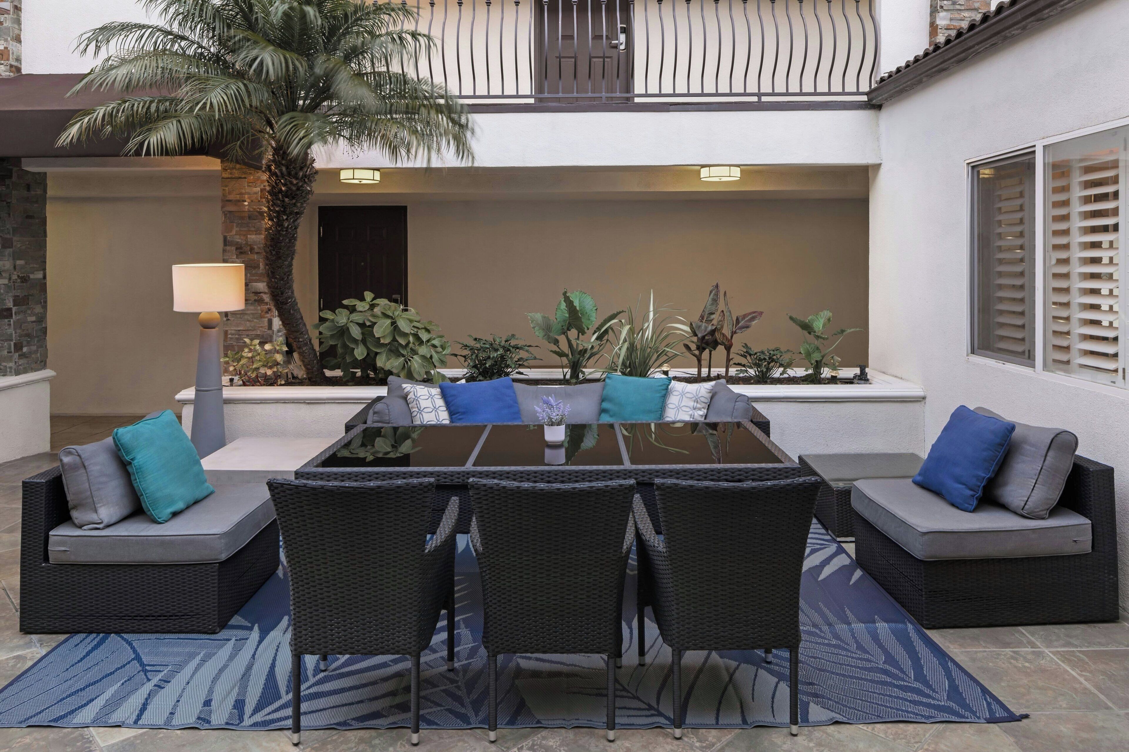 An outdoor patio with a glass-top table, black wicker chairs, and grey cushioned seating.
