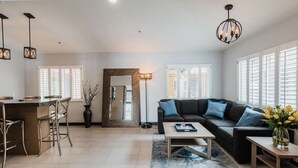 A spacious living area with a kitchen, a black leather sofa, a coffee table, and a dining area with bar stools. - City Express By Marriott Manhattan Beach (Manhattan Beach)