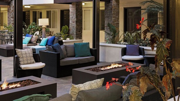 A well-lit outdoor seating area with multiple sofas and chairs, a fire feature, and potted plants. - City Express By Marriott Manhattan Beach (Manhattan Beach)