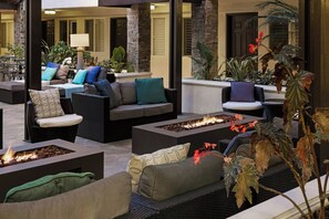 A well-lit outdoor seating area with multiple sofas and chairs, a fire feature, and potted plants. - City Express By Marriott Manhattan Beach (Manhattan Beach)