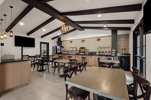 Ein modernes Restaurant mit freiliegenden Holzbalken, einer zentralen Verkaufstheke mit verschiedenen Speisen und mehreren Sitzbereichen mit Tischen und Stühlen.