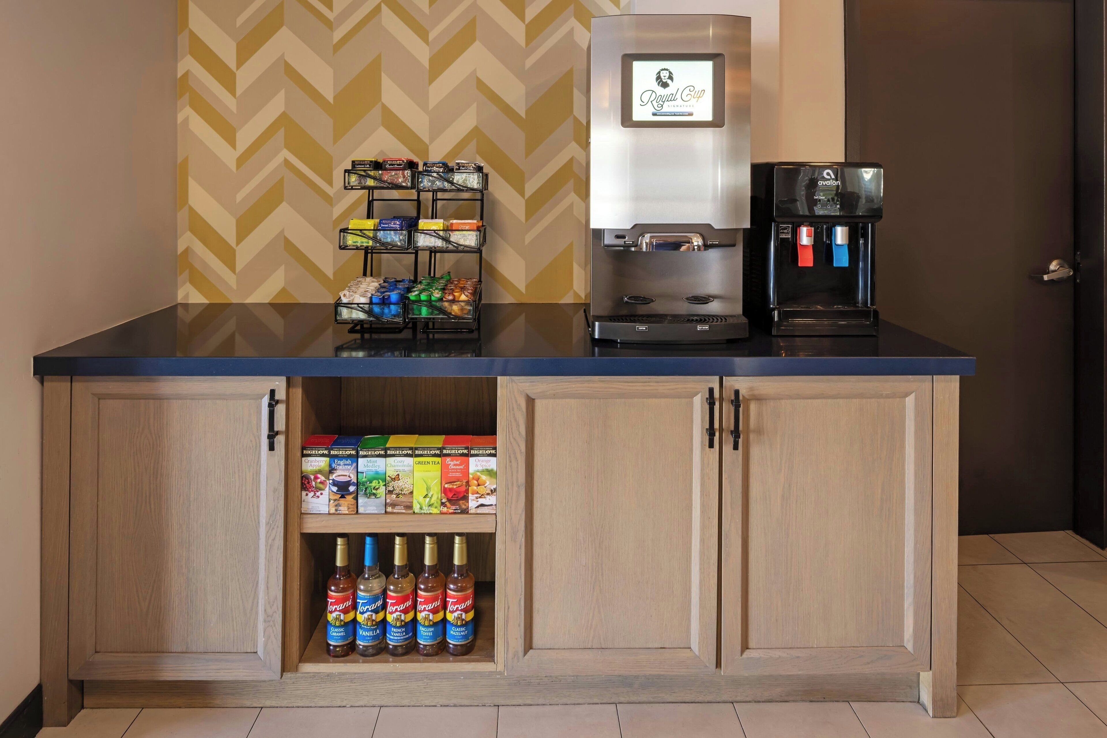 A kitchenette with a coffee machine, a beverage dispenser, and a shelf with packaged goods.
