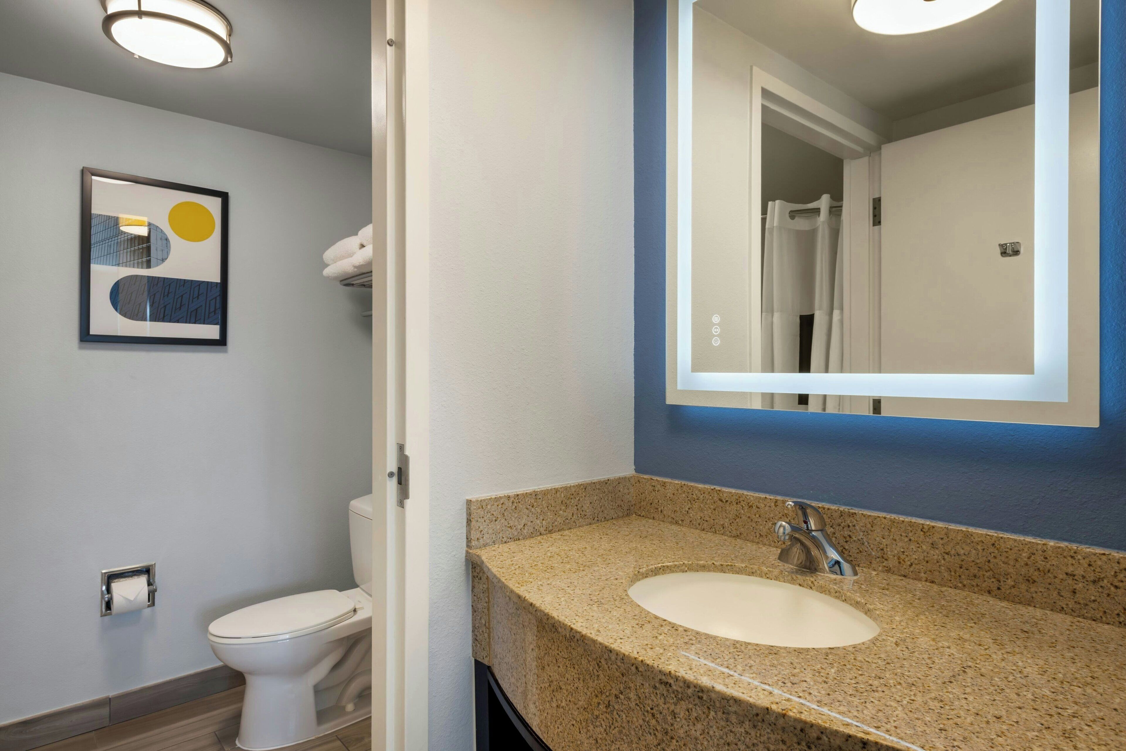 A modern bathroom with a white toilet, a granite countertop sink, and a large mirror.