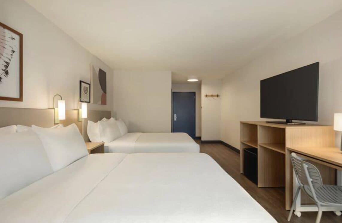 A hotel room with two beds, a desk with a TV, and a chair.