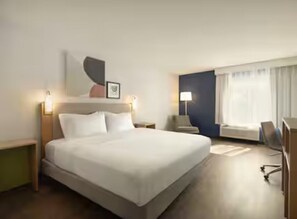 A hotel room with a large bed, bedside tables, a desk, and a chair.