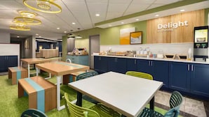 A modern dining area with tables and chairs, a kitchen counter, and a sign that reads "Delight in the day".