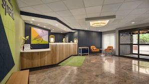 A reception area with a wooden reception desk, a green rug, and two orange chairs.