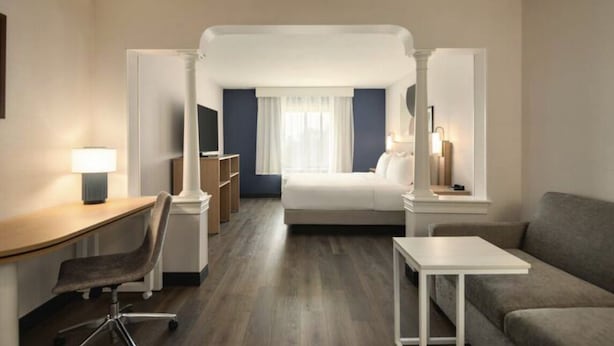 A hotel room with a desk, chair, bed, and a sofa.