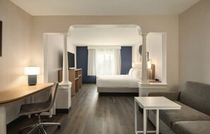 A hotel room with a desk, chair, bed, and a sofa.
