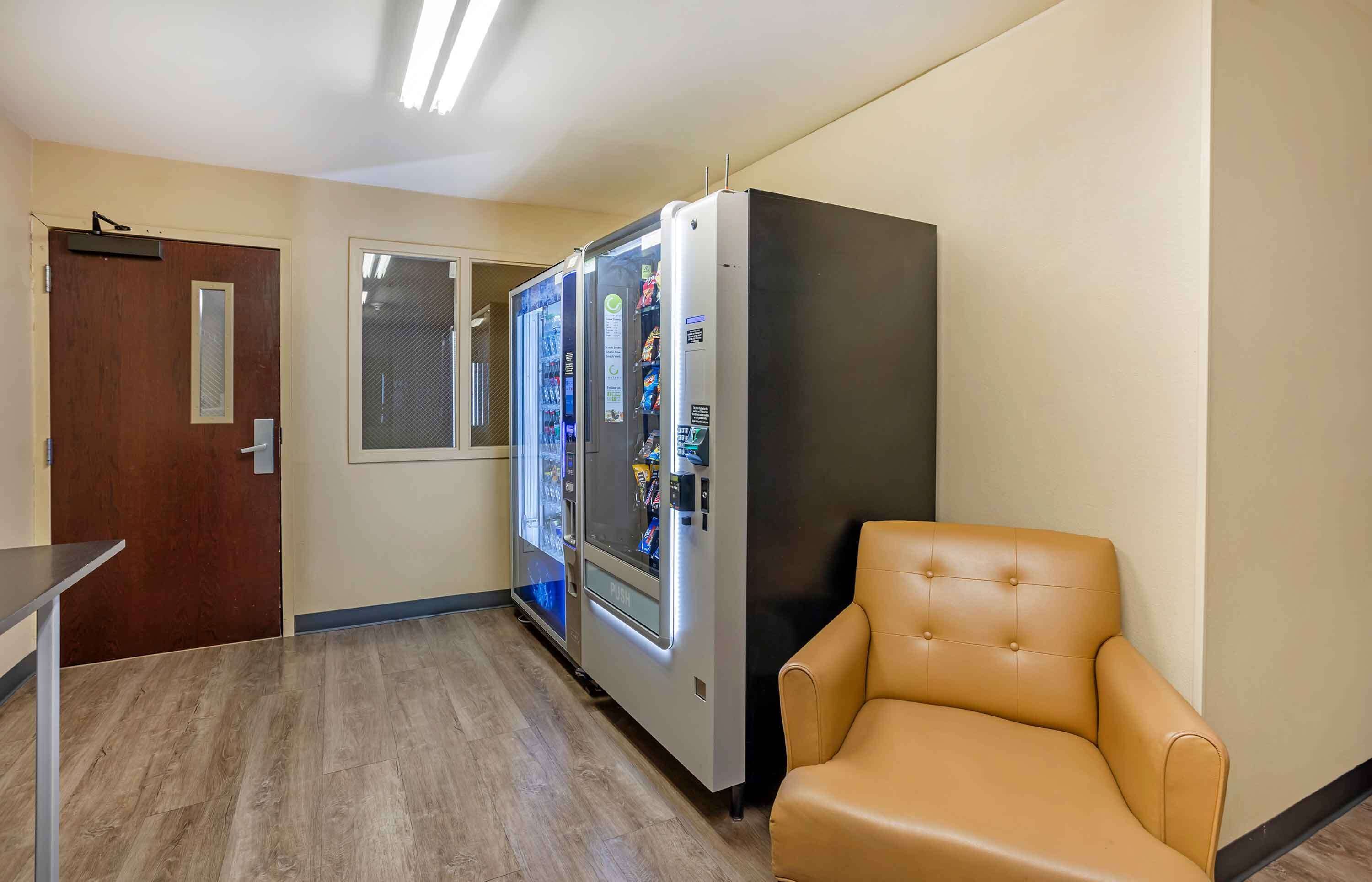 A hallway with a vending machine, a door, and a leather chair.