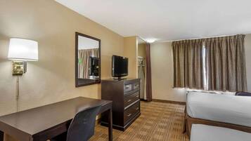 Quarto de hotel com escrivaninha, cadeira, televisão, cômoda e cama.