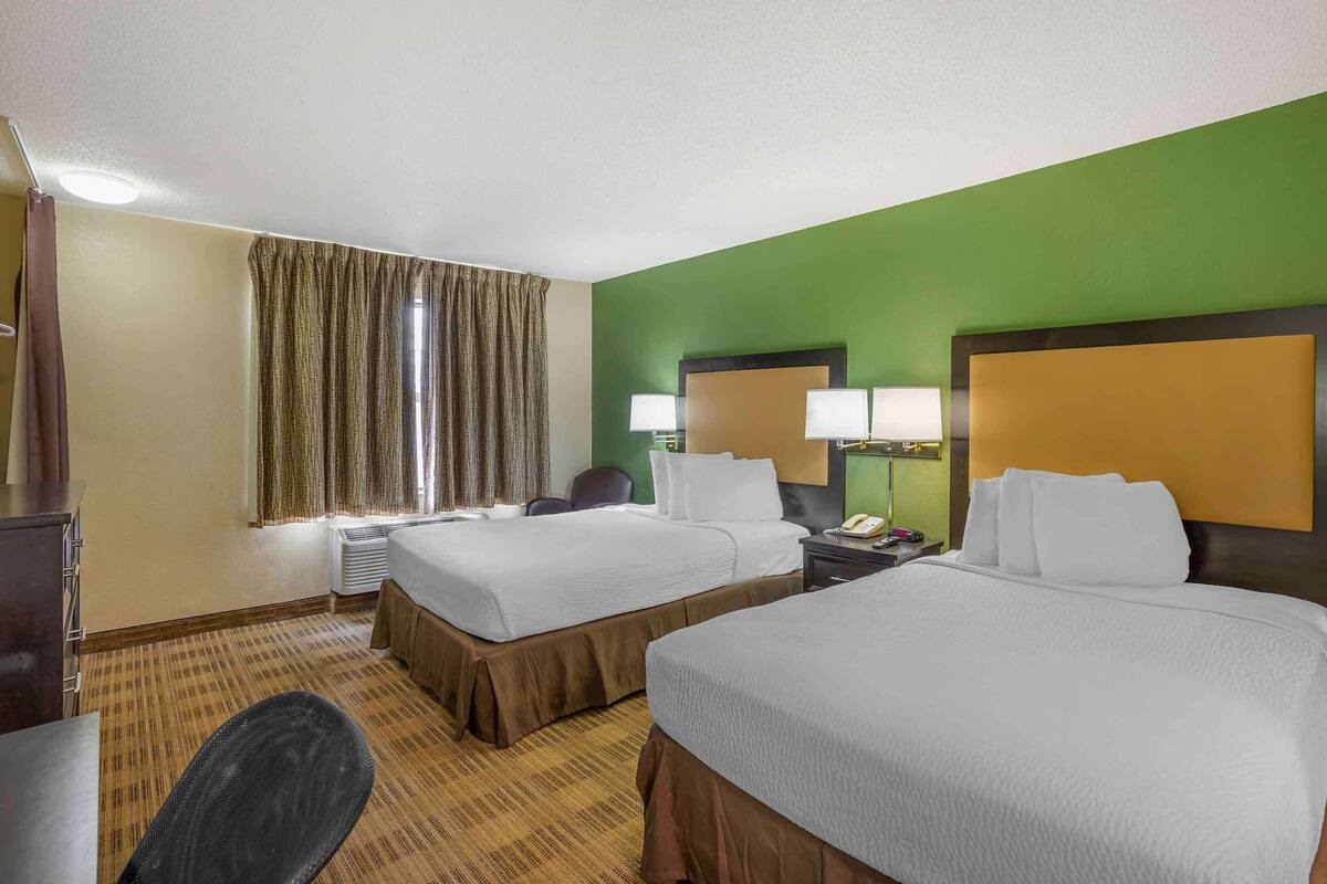 A hotel room with two beds, a desk, a chair, a telephone, and a window with curtains.