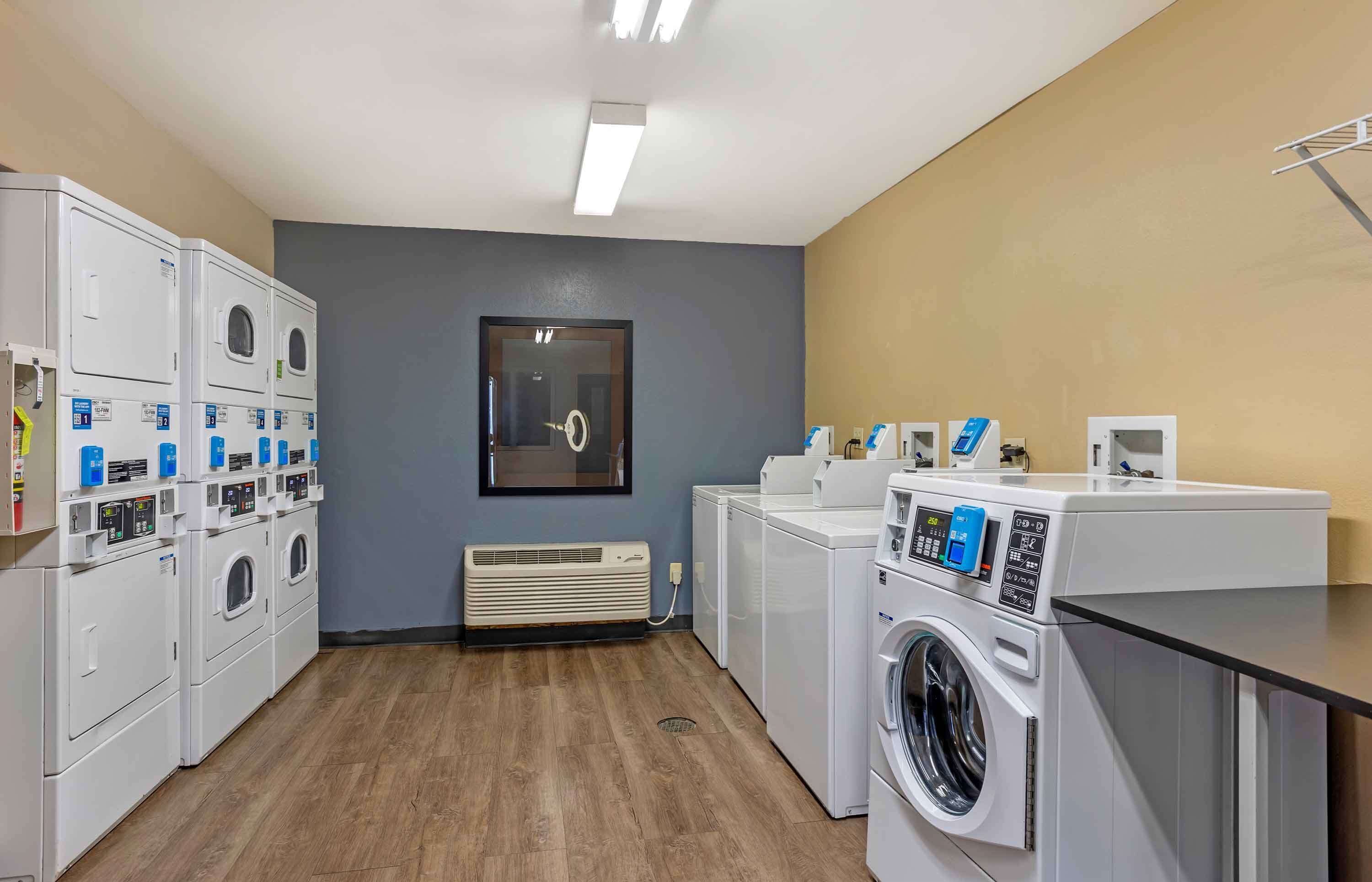 Uma lavanderia com várias máquinas de lavar e secar, uma unidade de ventilação e um espelho na parede.