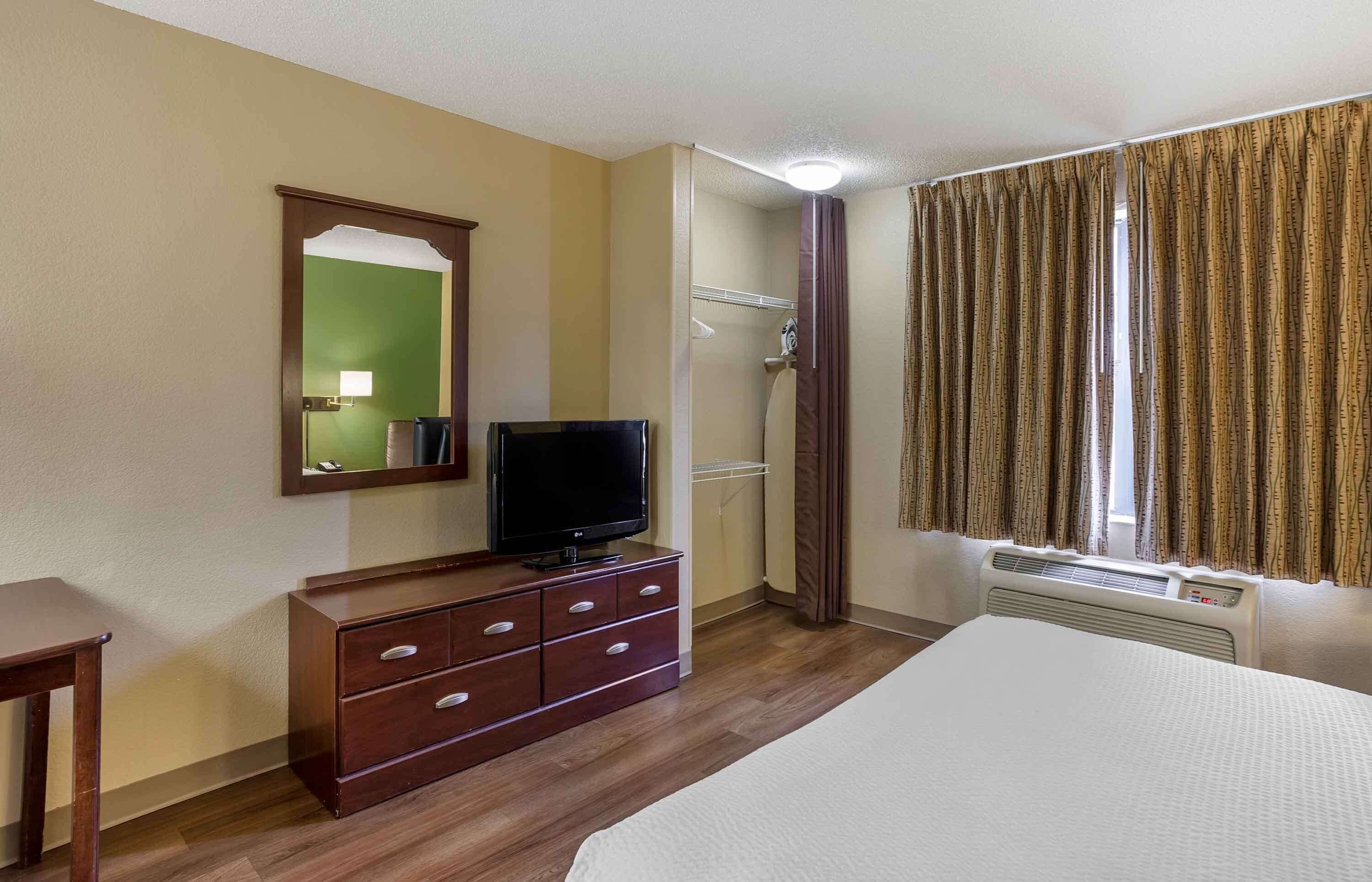 A hotel room with a bed, a TV on a wooden dresser, a shower, and curtains.
